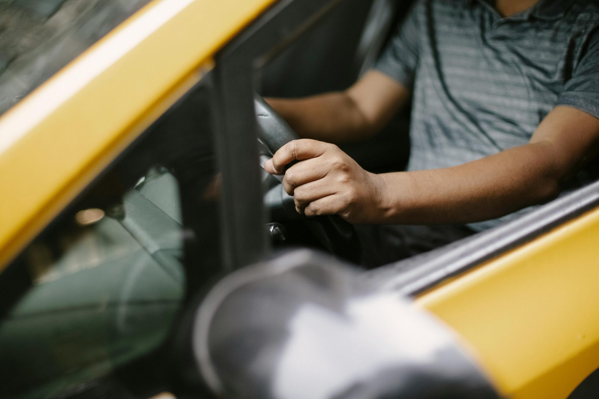 From above of crop unrecognizable male in polo shirt driving yellow cab on city street in daytime